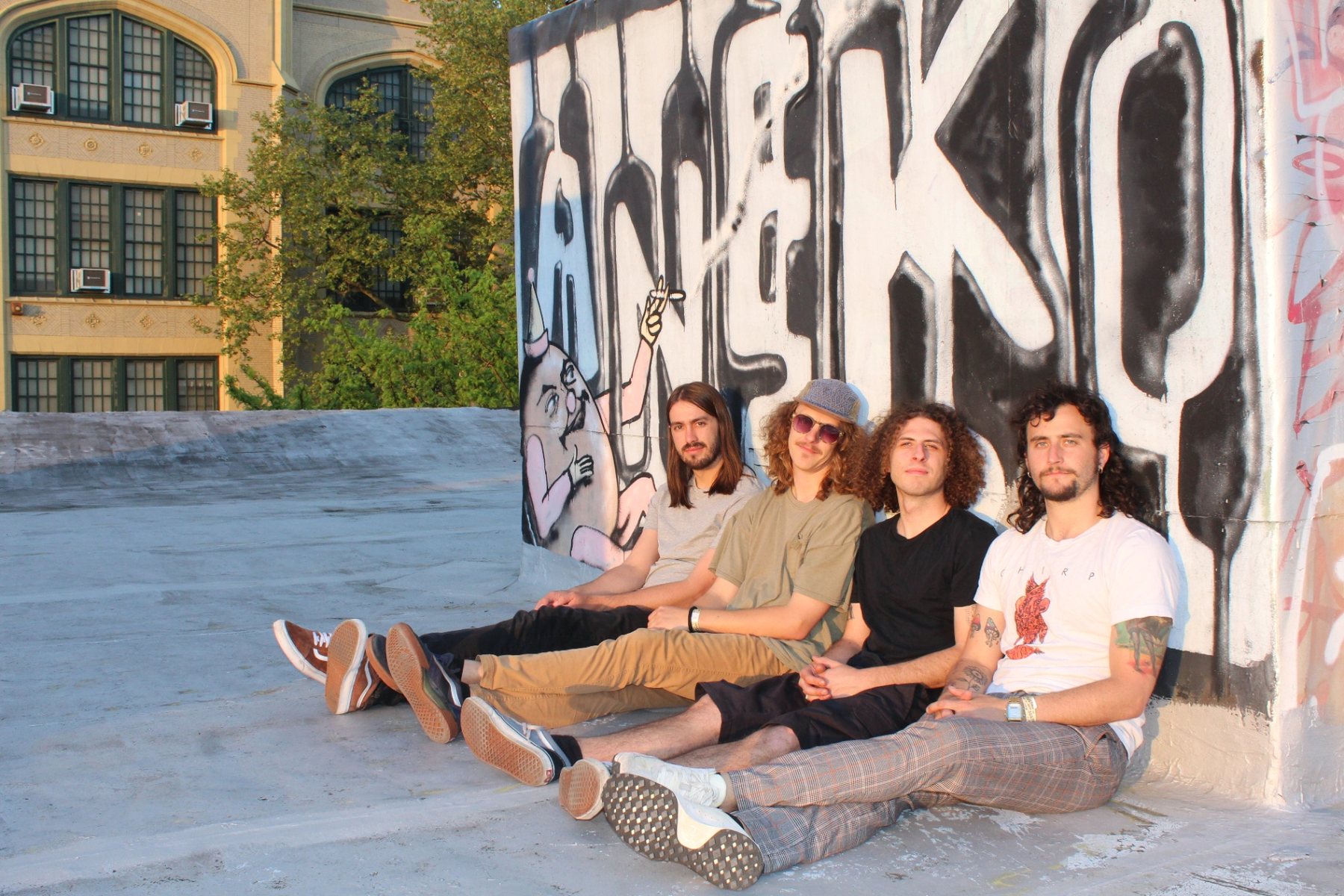 Sqwerv — the four of them sitting against a graffitied rooftop wall in Denver